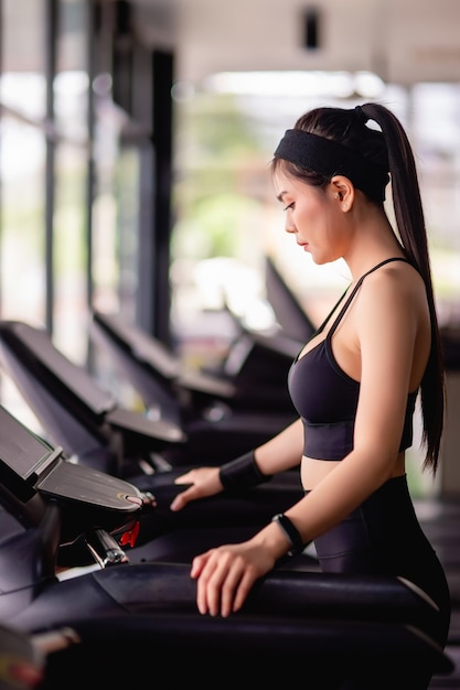 Young beautiful woman wearing sportswear, Sweat-proof fabric and smartwatch standing on treadmill warm up before run to workout in modern gym