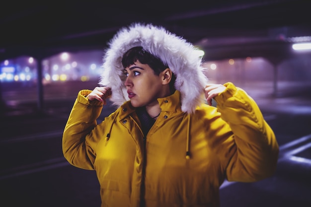 Free photo young beautiful woman wearing a yellow winter coat with a blurred city at night