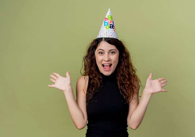 Young beautiful woman with curly hair in a holiday cap happy and excited birthday party concept  over light