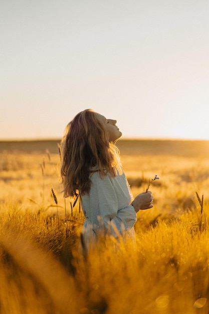 young beautiful woman with long blond hair in a white dress on a wheat field in the early morning at sunrise. Summer is the time for dreamers, flying hair, a woman running across the field in the rays