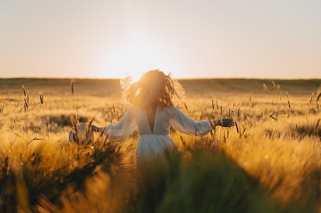 Free photo young beautiful woman with long blond hair in a white dress on a wheat field in the early morning at sunrise. summer is the time for dreamers, flying hair, a woman running across the field in the rays