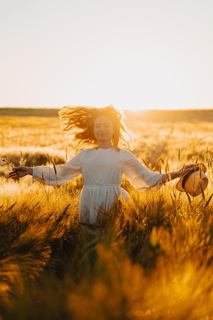 Free photo young beautiful woman with long blond hair in a white dress on a wheat field in the early morning at sunrise. summer is the time for dreamers, flying hair, a woman running across the field in the rays