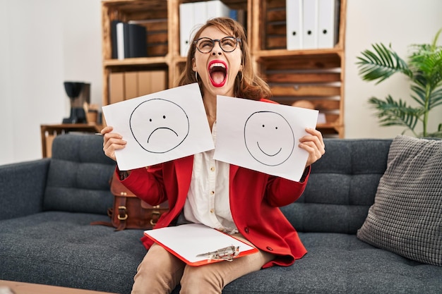 Free photo young beautiful woman working on depression holding sad to happy emotion paper angry and mad screaming frustrated and furious, shouting with anger looking up.