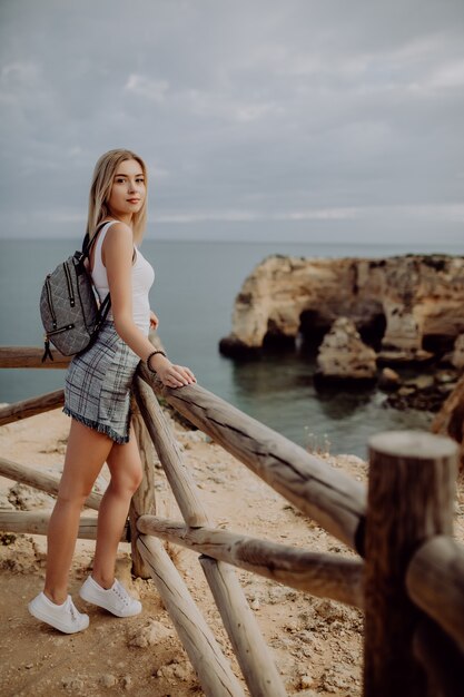 Young beauty blonde Woman traveler looking at the sea and cliff on beautiful Portugal beach.