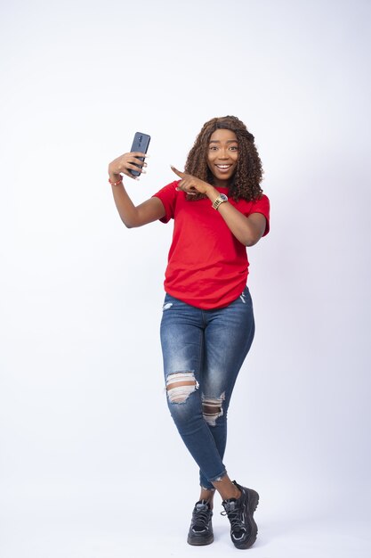 Young black lady holding her phone and pointing to it with excitement on her face