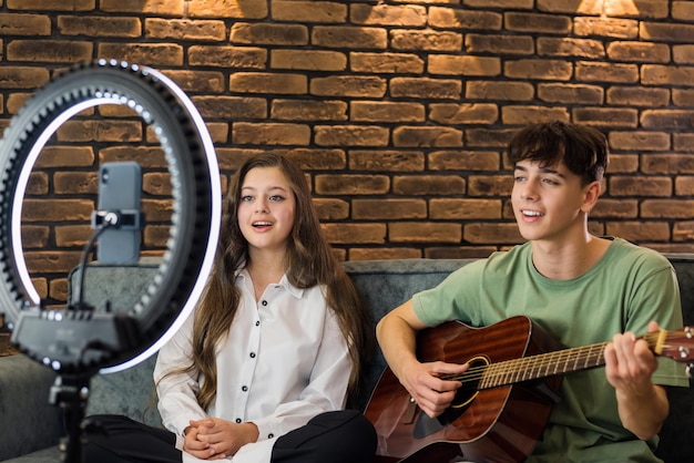 Free photo young blogger influencers shooting themselves while singing and playing guitar