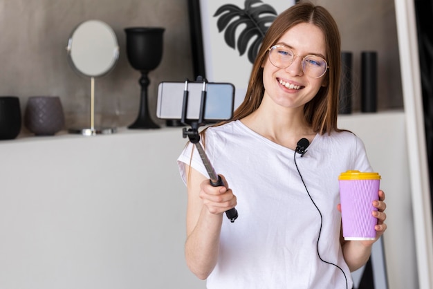 Young blogger recording with smartphone holding a travel mug