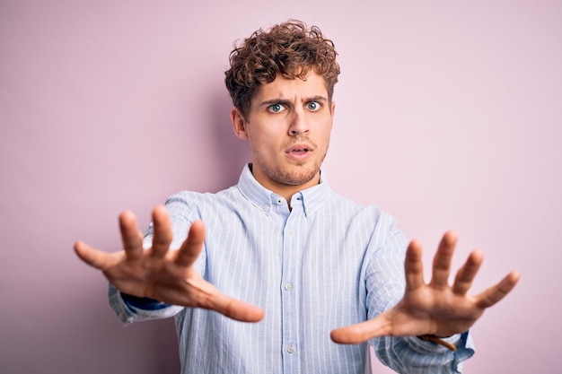 Free photo young blond handsome man with curly hair wearing striped shirt over white background doing stop gesture with hands palms angry and frustration expression