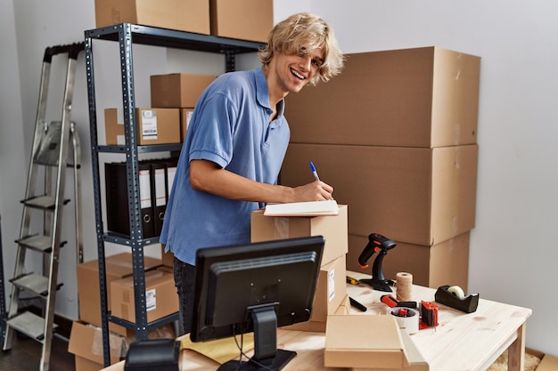 Free Photo young blond man ecommerce business worker using laptop writing on notebook at office