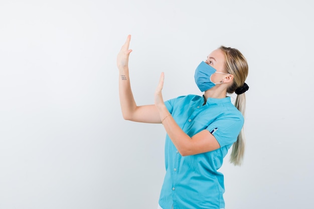 Young blonde female in casual clothes, mask raising hands to defend herself