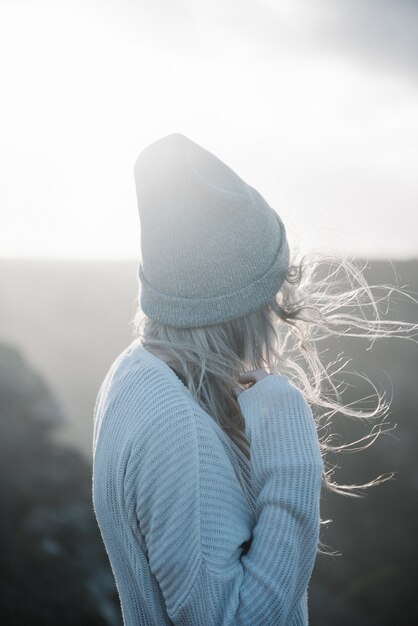 Young blonde female with a hat walking on the beach in a windy weather