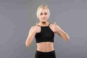 Free photo young blonde fit sporty girl woman thumbs up in black sportswear demostrate her strong muscular body