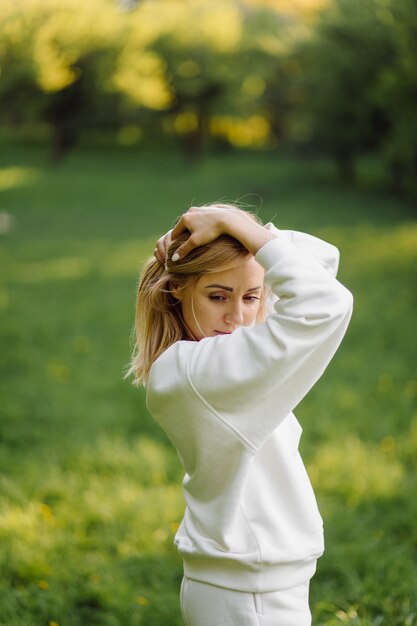 Young blonde girl is wearing a white hoodie smiling and walking in the woods