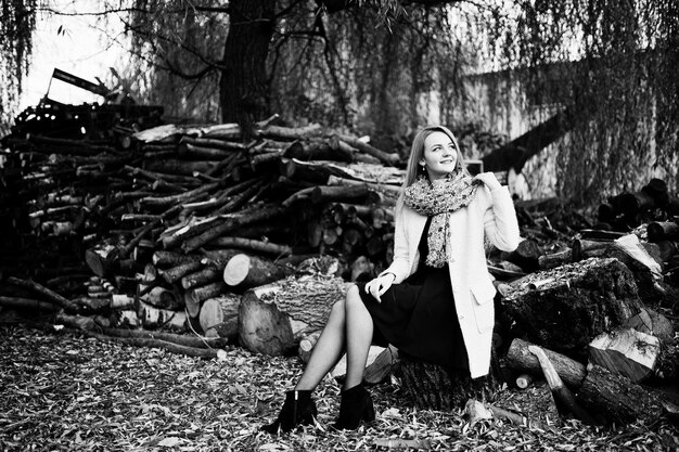 Young blonde girl at pink coat posed against wooden stumps background