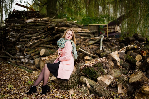 Free photo young blonde girl at pink coat posed against wooden stumps background