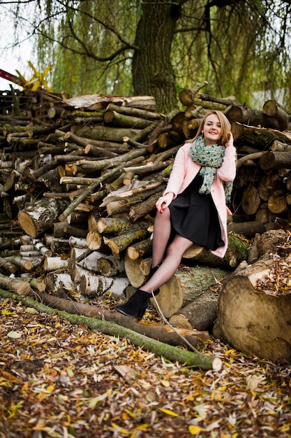 Free photo young blonde girl at pink coat posed against wooden stumps background