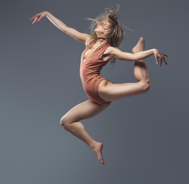 Young blonde graceful ballerina dances and jumps in a studio. Isolated on a gray background.