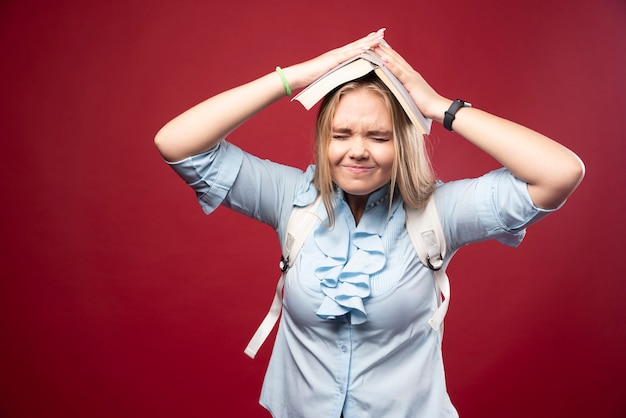 Free photo young blonde student woman holds her book at her head and looks tired and confused.