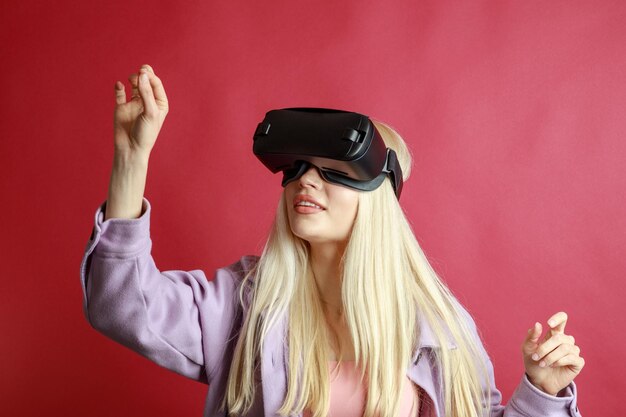 Young blonde wears VR glasses and stand on red background