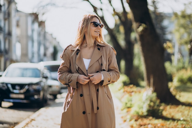 Free photo young blonde woman in beige coat walking in the street