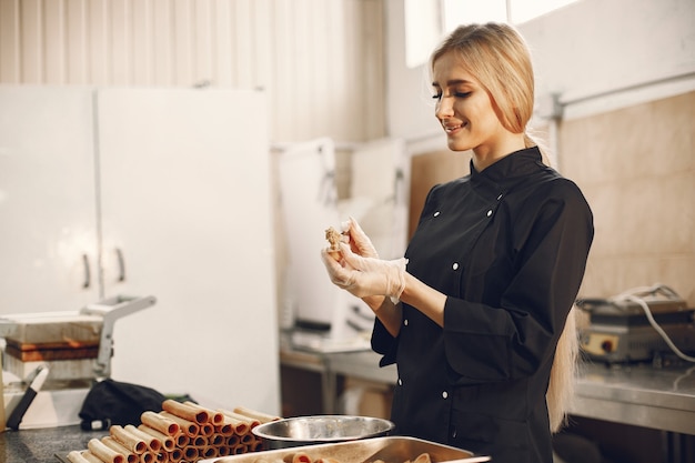 Free Photo young blonde woman in black uniform in kitchen of restaurant preparing different sweets and cookies.