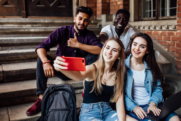 Free photo young blonde woman making selfie with her friends students, while they are sitting on stairs.