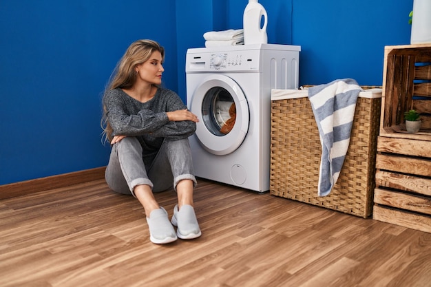 Free Photo young blonde woman sitting on the floor waiting for washing machine at laundry room