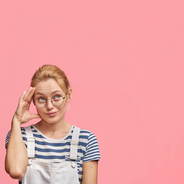 Free photo young blonde woman with round glasses and overalls