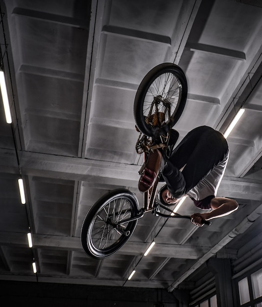 Free photo young bmx making crazy tricks on his bicycle in skatepark indoors. bmx freestyle.