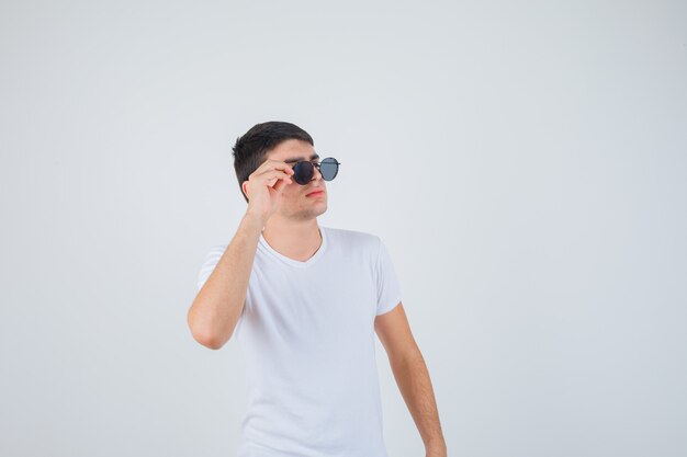 Young boy holding glasses, looking aside in t-shirt and looking cool , front view.