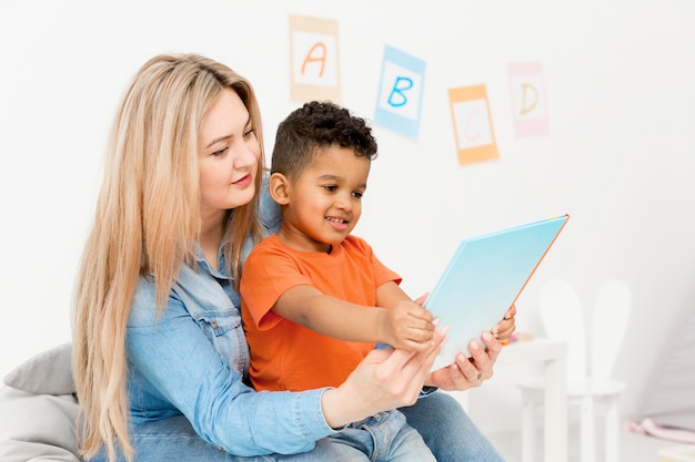 Young boy looking at notebook while being held by woman