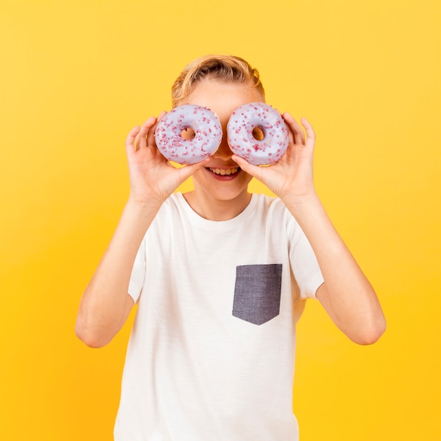 Free Photo young boy making glasses with doughnuts