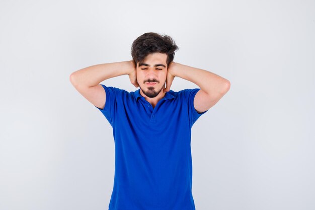 Young boy pressing hands on ears in blue t-shirt and looking harried. front view.