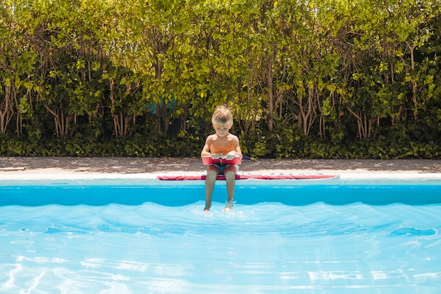 Young boy sitting by pool with book