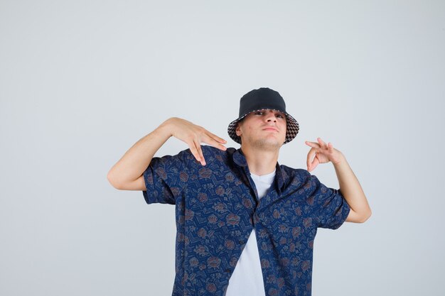 Young boy in white t-shirt, floral shirt, cap showing ok sign and doing hand gestures and looking confident