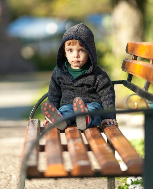 Free photo young boy with hoodie sitting on a wooden bench