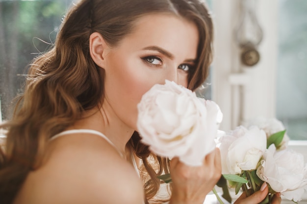 Free Photo young bride holds a bouquet of peonies siting on the windowsill in the bright morning