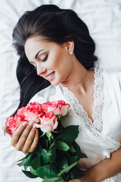 young brunette girl lays on her bed, in the morning and holds a Beautiful roses in her hands. Top view.