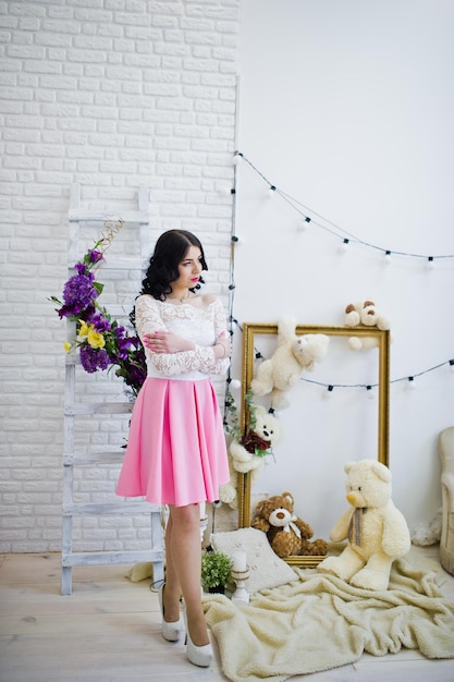 Free photo young brunette girl in pink skirt and white blouse posed indoor against room with toys bear