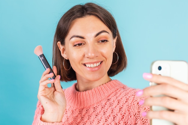 Free photo young brunette in pink sweater isolated on blue wall