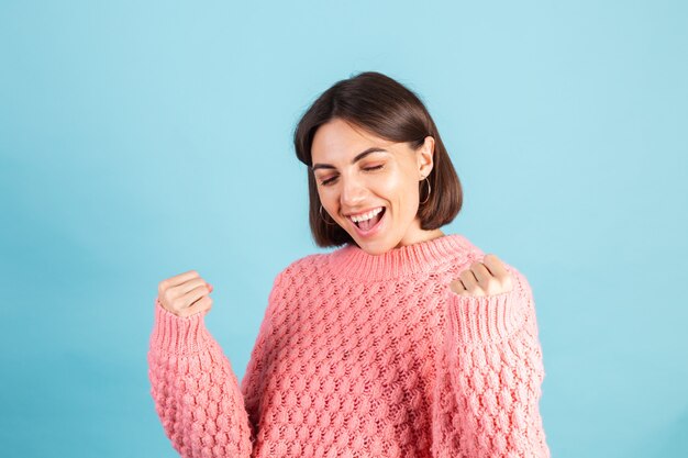 Young brunette in warm pink sweater isolated on blue wall