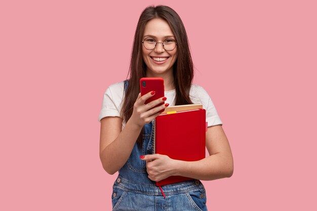 Young brunette woman in denim overalls holding notepads