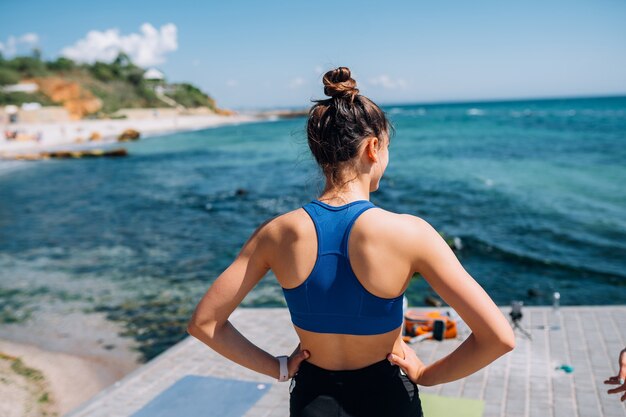 Young brunette woman wearing fitness outfit, stretching on pier