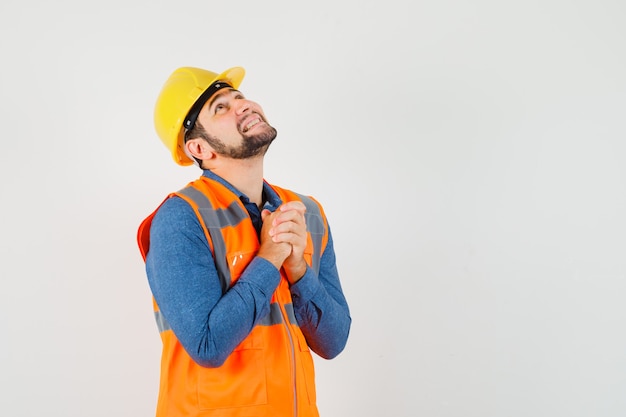 Young builder clasping hands in praying gesture in shirt