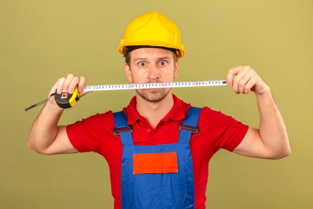 Free Photo young builder man in construction uniform and safety helmet holding tape-line with surprised face over isolated green wall