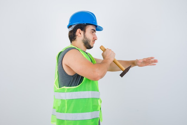 Young builder man remowing something with using hammer in workwear uniform and looking confident , front view.