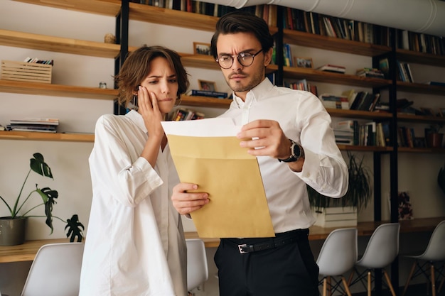 Young business colleagues thoughtfully reading envelope letter while working together in modern office