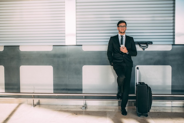 Young business man standing on the phone with the suitcase at the airport waiting for the flight xAxA