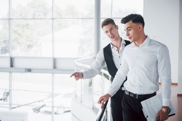 Young business people looking at documents and products standing at the office railing