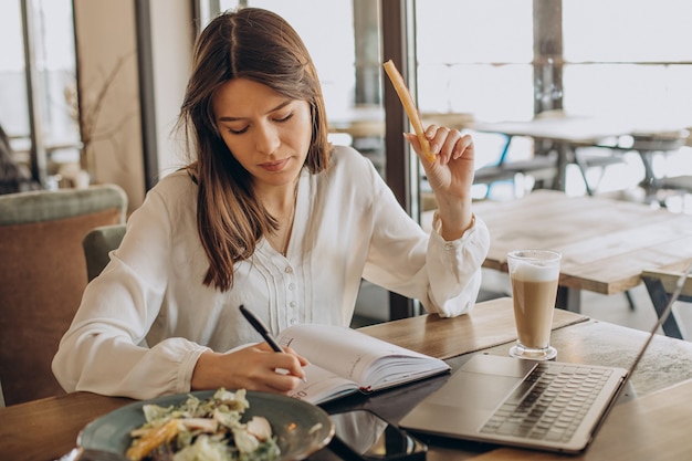 Young business woman having lunch in a cafe and working on computer